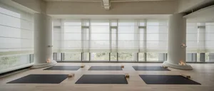 A yoga studio with modern interior design, featuring gray columns, wooden flooring, and black yoga mats.