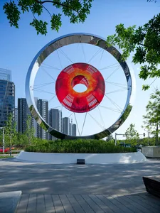 A modern urban sculpture featuring a red circular screen and a metallic circular frame.