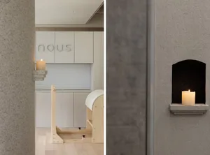 A minimalist office space with light wooden furniture and plaster walls, featuring a candle on a ledge.