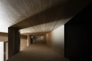 A modern, minimalist corridor featuring textured concrete walls and ceiling.
