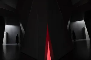 Two individuals standing in a modern black interior space with a glass wall and red light