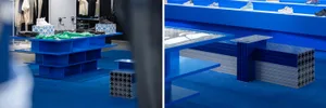 A modern retail display featuring blue metal tables, glass shelves, and fabric items for sale in a store.