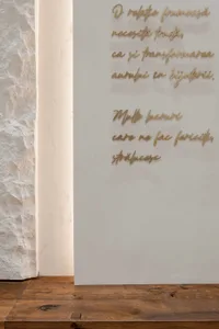 A wall with a quote displayed in cursive script, surrounded by a wooden floor and a textured stone wall.
