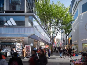 陽光普照的都市街景，綠樹聳立，人們在人行道上行走，兩旁商店林立。