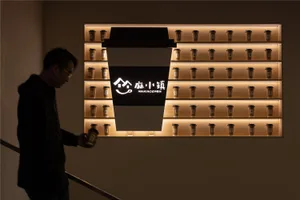 A coffee shop display featuring a large, illuminated coffee cup sign and numerous smaller coffee cups on shelves.