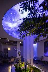 A futuristic exhibit featuring a projection of the galaxy, a metallic deer statue, and a tree.