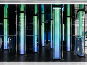 Modern clothing retail store with illuminated glass columns showcasing vibrant clothing displays.