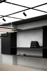A minimalist shelf with a textured concrete wall and black shelving units. Includes a black purse and beige towels.