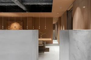 A modern restaurant interior features a textured concrete ceiling with minimal overhead lighting and a wooden dining table.