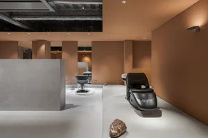 A minimalist interior space featuring concrete walls, a black leather massage chair, and large windows.