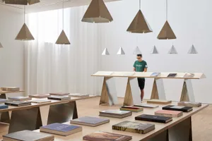A minimalist library space featuring wood tables, metal bookends, and paper books arranged on display.