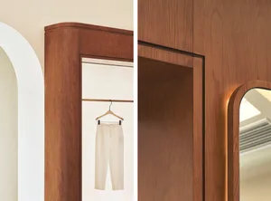 A minimalist clothing store interior with wooden panels, white trousers hanging on a metal rail, and an arched doorway.