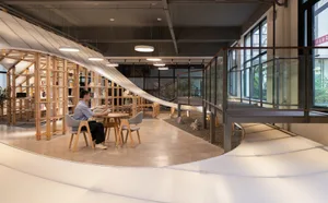 A minimalist library space featuring wooden tables, glass partitions, and concrete flooring.