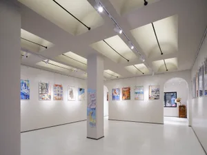 A modern art gallery with white walls, hanging paintings, and track lighting.