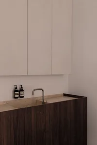Modern bathroom featuring wooden cabinets, white walls, and a stone countertop with a sink and faucet.