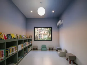 A minimalist reading room with concrete walls, wooden furniture, and a bookshelf filled with books.
