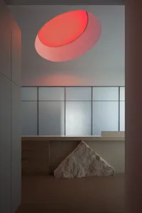 A minimalist bedroom with a prominent concrete stone and an oval-shaped window emitting warm light.