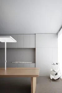 A minimalist workspace featuring a wooden table with a white lamp and a metal laundry rack with white bags.