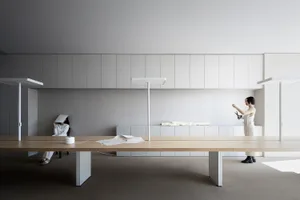 A modern office space featuring a minimalist desk with a light wooden surface and white elements in the background.