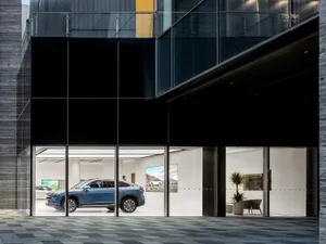 Modern car showroom with glass exterior and concrete interior featuring a blue SUV on display.