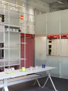 An industrial-style office space with metal shelving units and a long white desk with glassware.