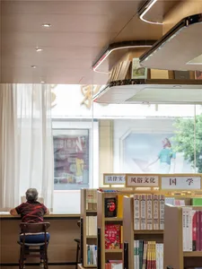 A modern library with a wooden staircase, white curtains, and bookshelves filled with books.