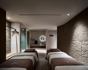 A modern spa room with concrete walls and two massage tables.