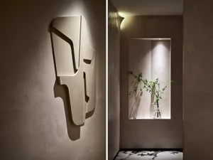 Minimalist interior design featuring textured concrete walls with geometric wall sculptures and a vase with greenery.
