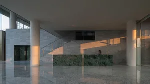 A modern lobby with marble flooring and walls, featuring a glass staircase and large windows.
