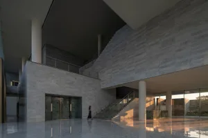 Modern interior lobby with marble walls and floors, white columns, and a person walking by the entrance.