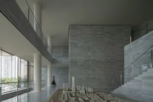 A modern interior space with concrete walls and flooring, featuring architectural models and high ceilings with large windows