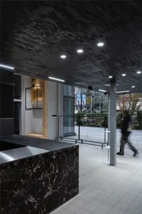 A modern lobby featuring a concrete ceiling and floor, with a reception desk and a view of the exterior.