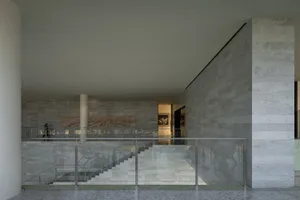 A modern hotel lobby featuring marble walls and floors, with a staircase and glass railings.