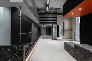 A modern office lobby with a minimalist design featuring concrete walls, floors, and ceiling, with orange accents.