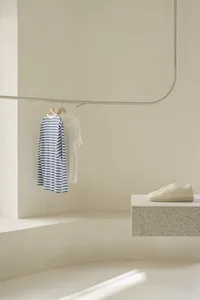 A minimalist white interior features a concrete bench with a pair of sneakers placed on it, a white tee, a blue and white str