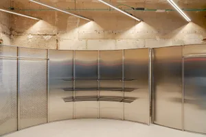 A large, metal wall display inside an industrial exhibition space, featuring a wave-like design and multiple shelves.