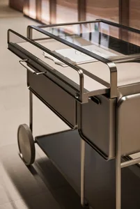 A modern, industrial-style metal cart with a glass top and leather-like drawer.