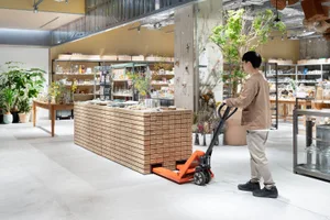 Man pushing a hand pallet truck in a modern retail store interior with wood and steel elements.