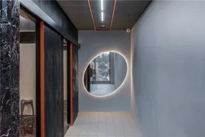 A modern corridor featuring concrete walls and flooring, with an oval-shaped mirror embedded in the wall.