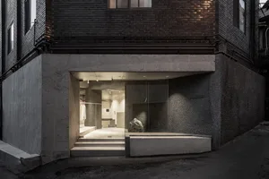 Concrete storefront with glass door and steps leading into a warmly lit interior.