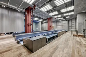 A spacious workshop featuring industrial design elements, such as metal and concrete structures, and a metallic conveyor syst