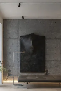 A minimalist living space with a concrete wall, black wall art, and a leather ottoman.