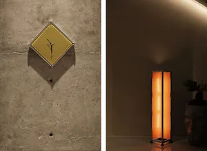 A square, modern pendant lamp with a perforated metal shade hangs from a concrete wall.