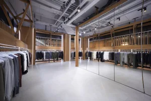 A modern clothing shop with wooden shelves displaying apparel in a glass-walled interior.