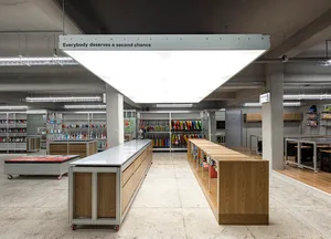 A spacious industrial workshop with concrete walls and flooring, featuring rolling carts, shelves, and hanging clothing racks