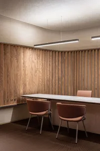 Modern office space featuring wooden panel walls and a long desk with cushioned chairs.