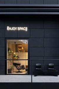 A modern retail storefront with a black concrete exterior, featuring a glass door and black furniture outside.