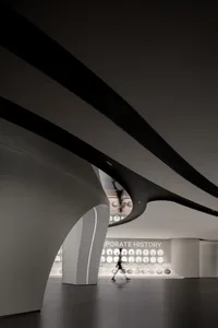 A minimalist, black and white corporate exhibition space with curved architectural elements and a focus on corporate history.