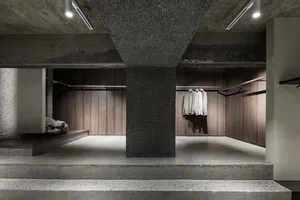 A minimalist clothing boutique with concrete flooring and wooden clothing racks.
