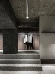 Modern clothing shop interior with concrete and wooden surfaces, featuring clothing racks.